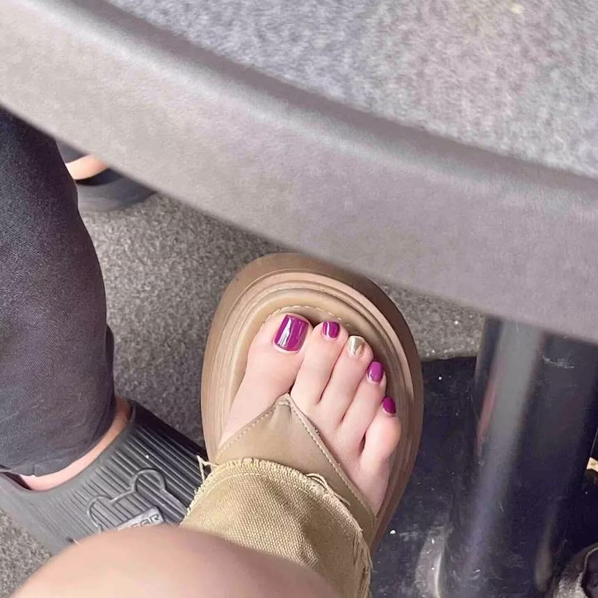 Vibrant summer pedicure trends featuring light blue nail polish with white polka dots on barefoot toes, adorned with a delicate shell anklet, against a sandy shore background.