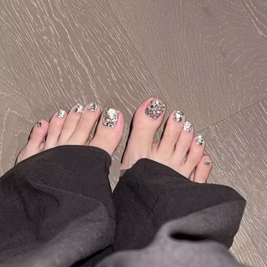 Vibrant summer pedicure trends featuring light blue nail polish with white polka dots on barefoot toes, adorned with a delicate shell anklet, against a sandy shore background.