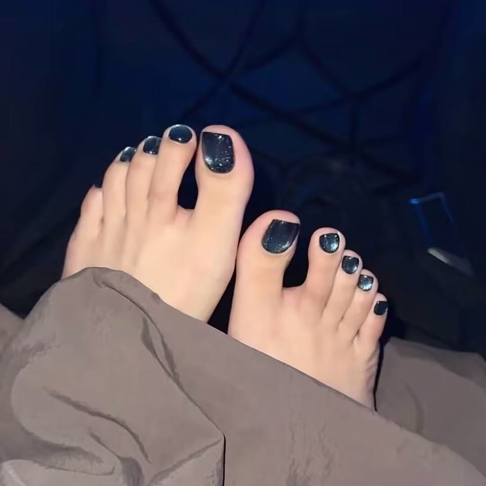  Close-up view of whimsical fairy pedicure designs featuring delicate glitter gradients, tiny floral accents, and ethereal wing motifs on toenails, in soft pastel and iridescent colors.