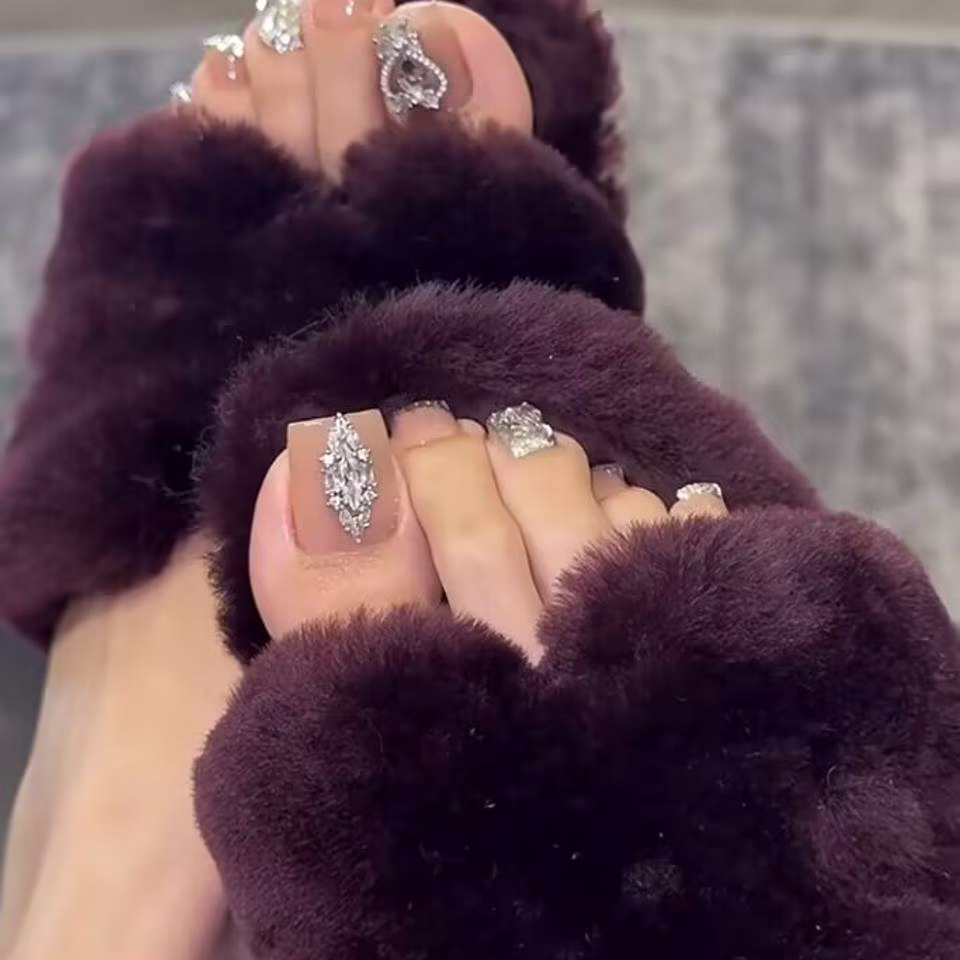  Close-up view of whimsical fairy pedicure designs featuring delicate glitter gradients, tiny floral accents, and ethereal wing motifs on toenails, in soft pastel and iridescent colors.