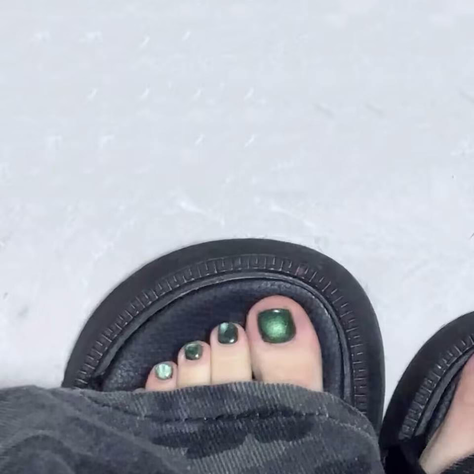  Close-up view of whimsical fairy pedicure designs featuring delicate glitter gradients, tiny floral accents, and ethereal wing motifs on toenails, in soft pastel and iridescent colors.