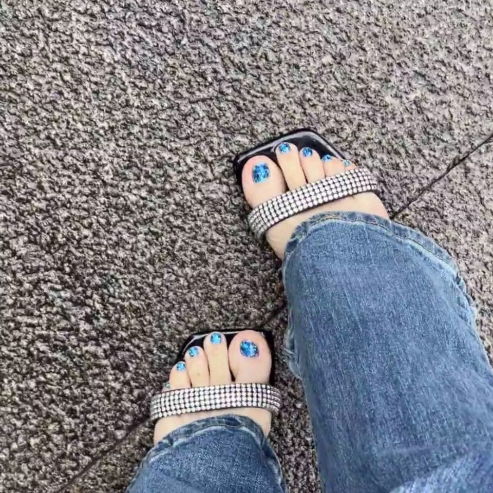  Close-up view of whimsical fairy pedicure designs featuring delicate glitter gradients, tiny floral accents, and ethereal wing motifs on toenails, in soft pastel and iridescent colors.